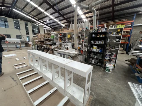 Long white bench structure beside roller supports, shelving and the factory work area.