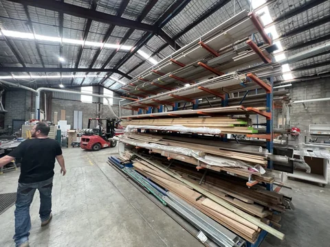 Long-stock storage racks beside the main warehouse aisle, with workshop equipment further inside.