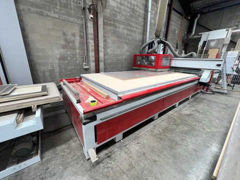 Large red-and-white flat-bed workshop machine beside an extraction unit and upright sheet materials.