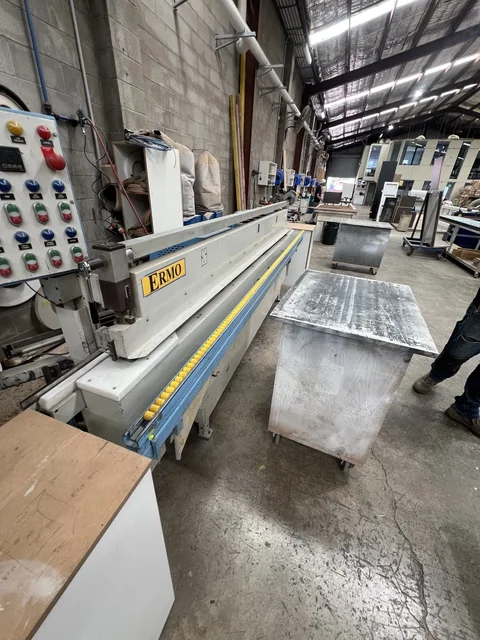 Long industrial processing machine with a control panel and adjoining workshop storage.