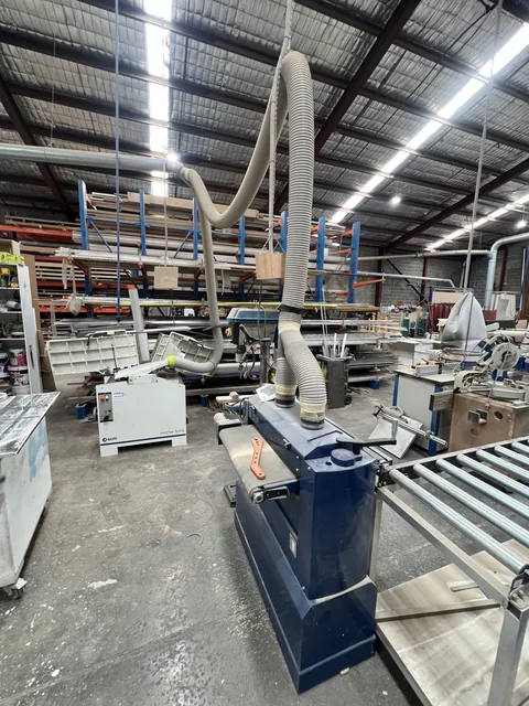 Workshop machinery with roller supports, overhead extraction ducting and storage racks in the background.