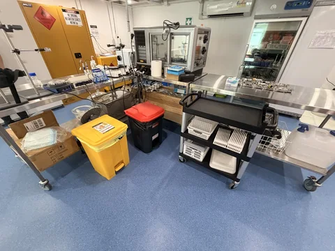 Stainless steel laboratory benches, storage shelves and tall equipment within the work area.