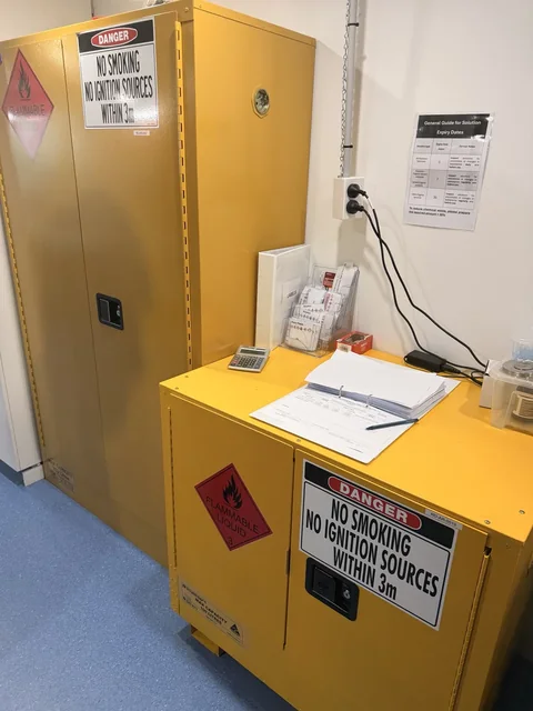 Yellow laboratory safety-storage cabinets with warning labels and nearby paperwork.