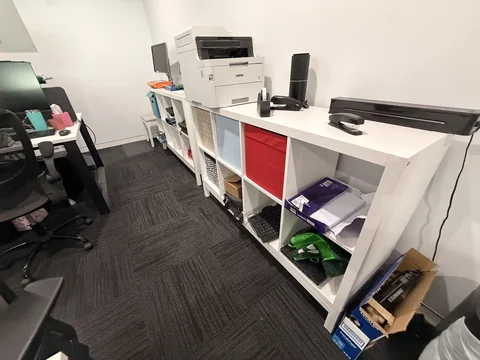 Office print and storage area with a printer, open shelving and equipment on the work surface.