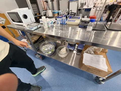 Stainless steel laboratory bench on castors with instruments, glassware and lower-shelf storage.