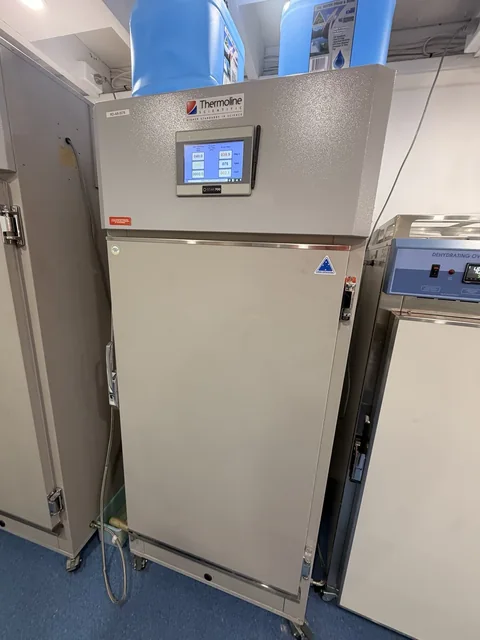 Front view of a tall laboratory cabinet with a digital control panel and containers stored above.