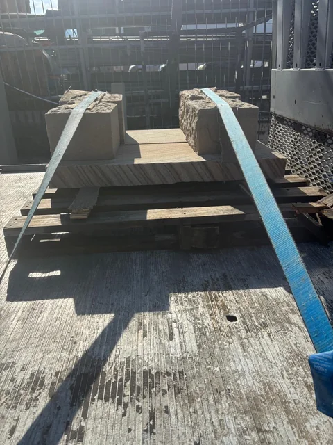 An inverted sandstone bench assembly resting on timber supports and secured with blue restraints on the truck tray.
