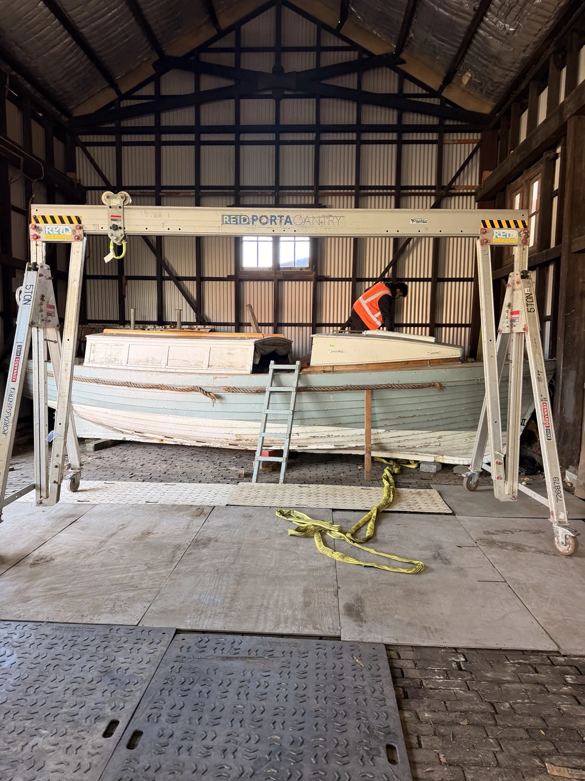 Boat beneath a mobile gantry inside the heritage building, with floor-protection sheets across the working route.