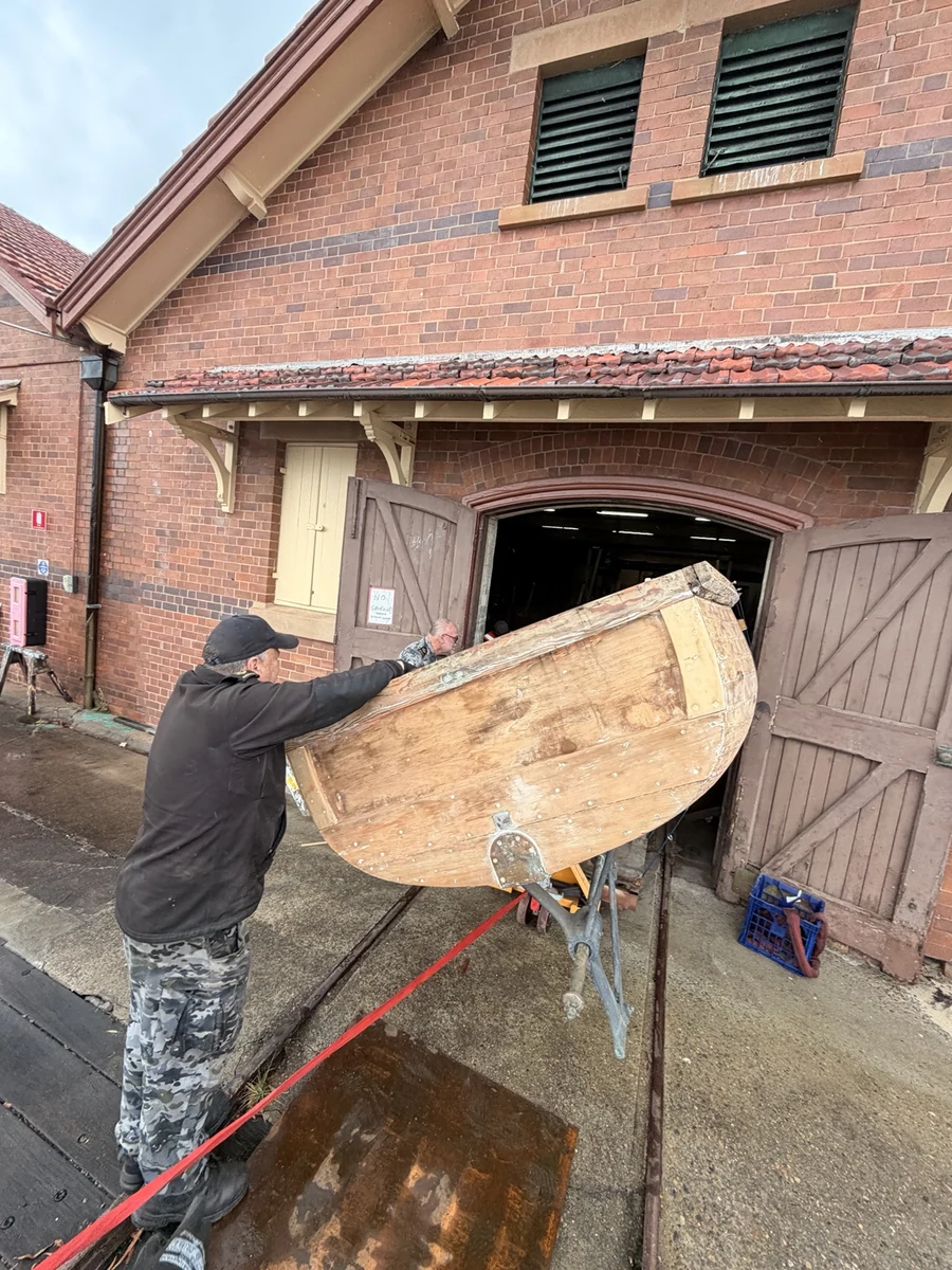 JB crew guiding the angled timber boat through the warehouse doorway