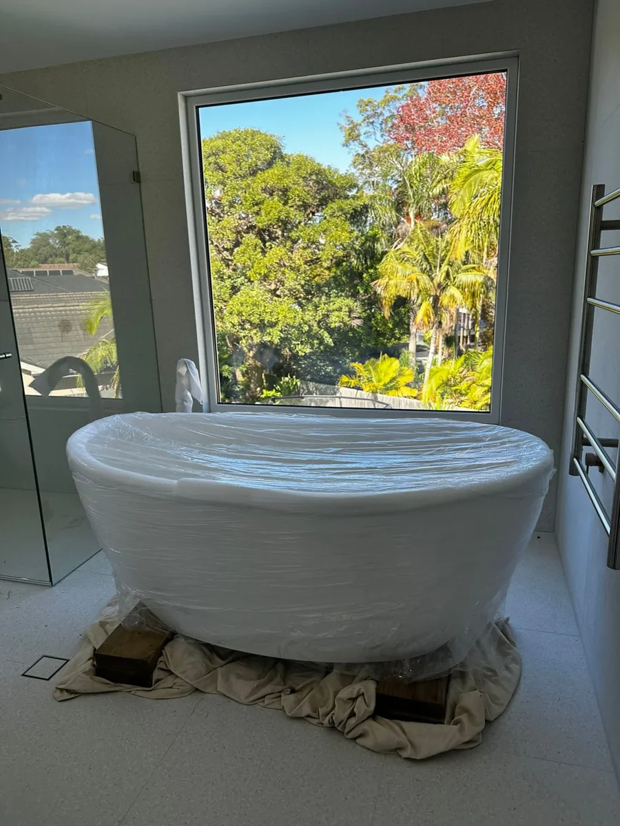 White freestanding bath with clear wrapping resting on padding in a bright room