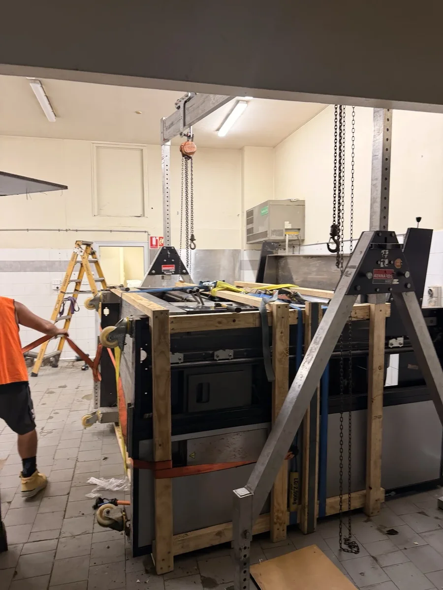 Commercial pizza oven enclosed by timber support framing beneath a gantry with chain hoists