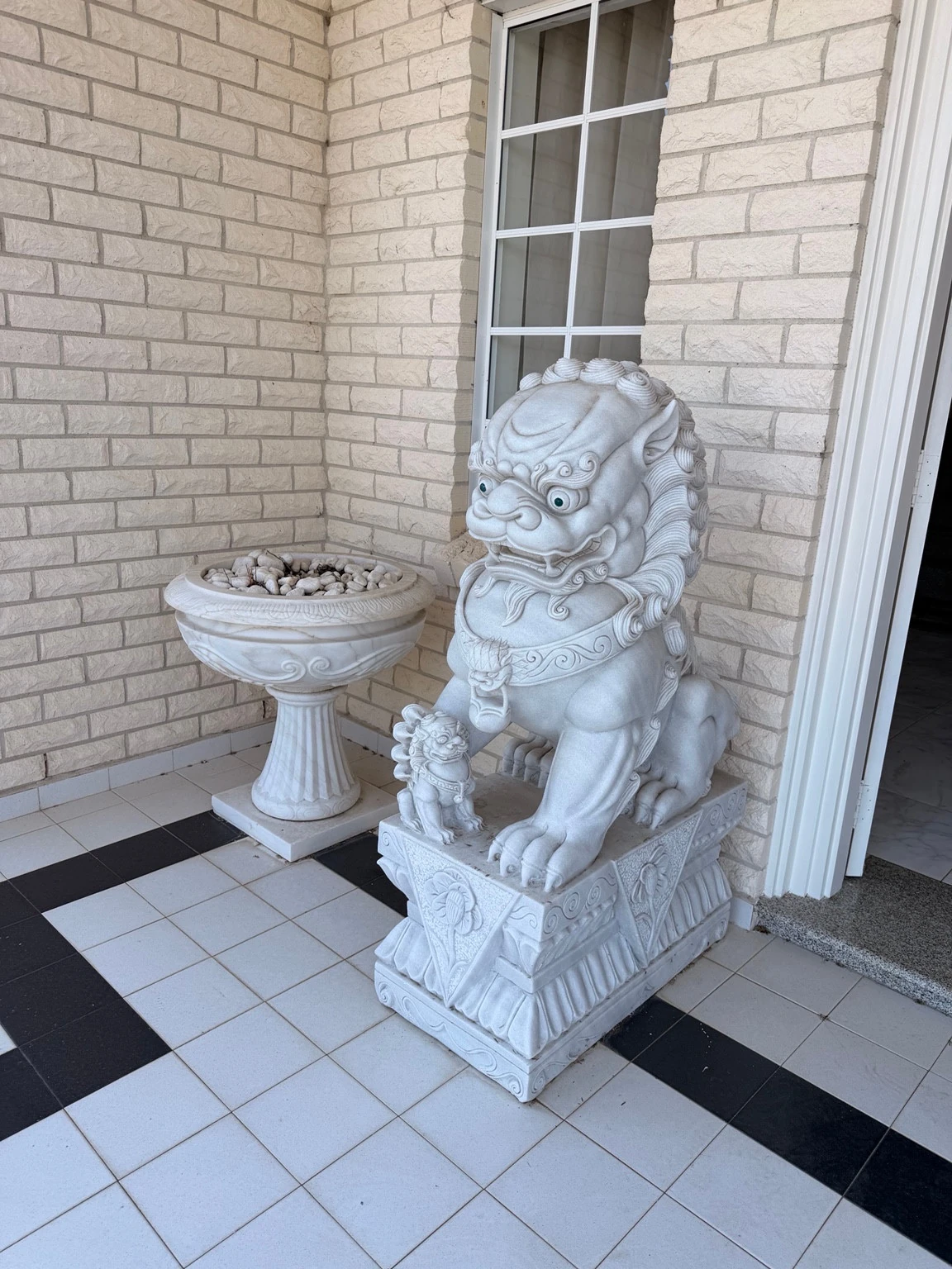 Carved guardian lion with a smaller lion figure on a rectangular base beside a pedestal planter